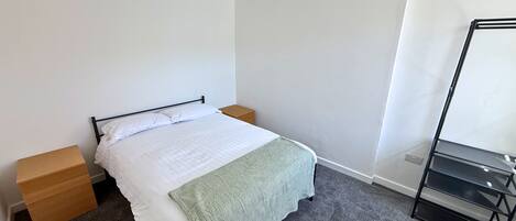 Une chambre à coucher comprenant un lit, une table de chevet, une commode, un miroir et un sol recouvert d’une moquette.