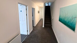 Un couloir avec un sol recouvert de moquette, des murs blancs, une porte, un escalier et un tableau.