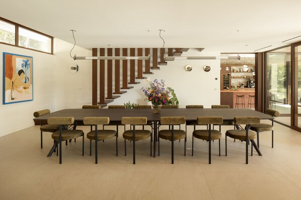 A modern dining area with a long table and chairs, a staircase, and a kitchen visible through an open door.