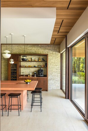 A modern kitchen with a stone wall, wooden ceiling, and large windows.