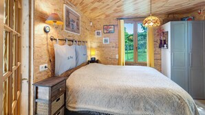 Une pièce aux murs lambrissés, comprenant un lit, une table de chevet, une lampe, une armoire et une fenêtre donnant sur un paysage verdoyant.