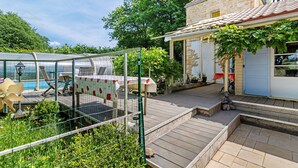 Une maison avec une façade en pierre, une terrasse en bois et une serre en verre.
