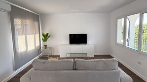 A modern living room with a grey sofa, a TV on a white stand, and a plant. - Charming El Paraiso Apt with Gibraltar Views Near Puerto Banus (El Paraíso)