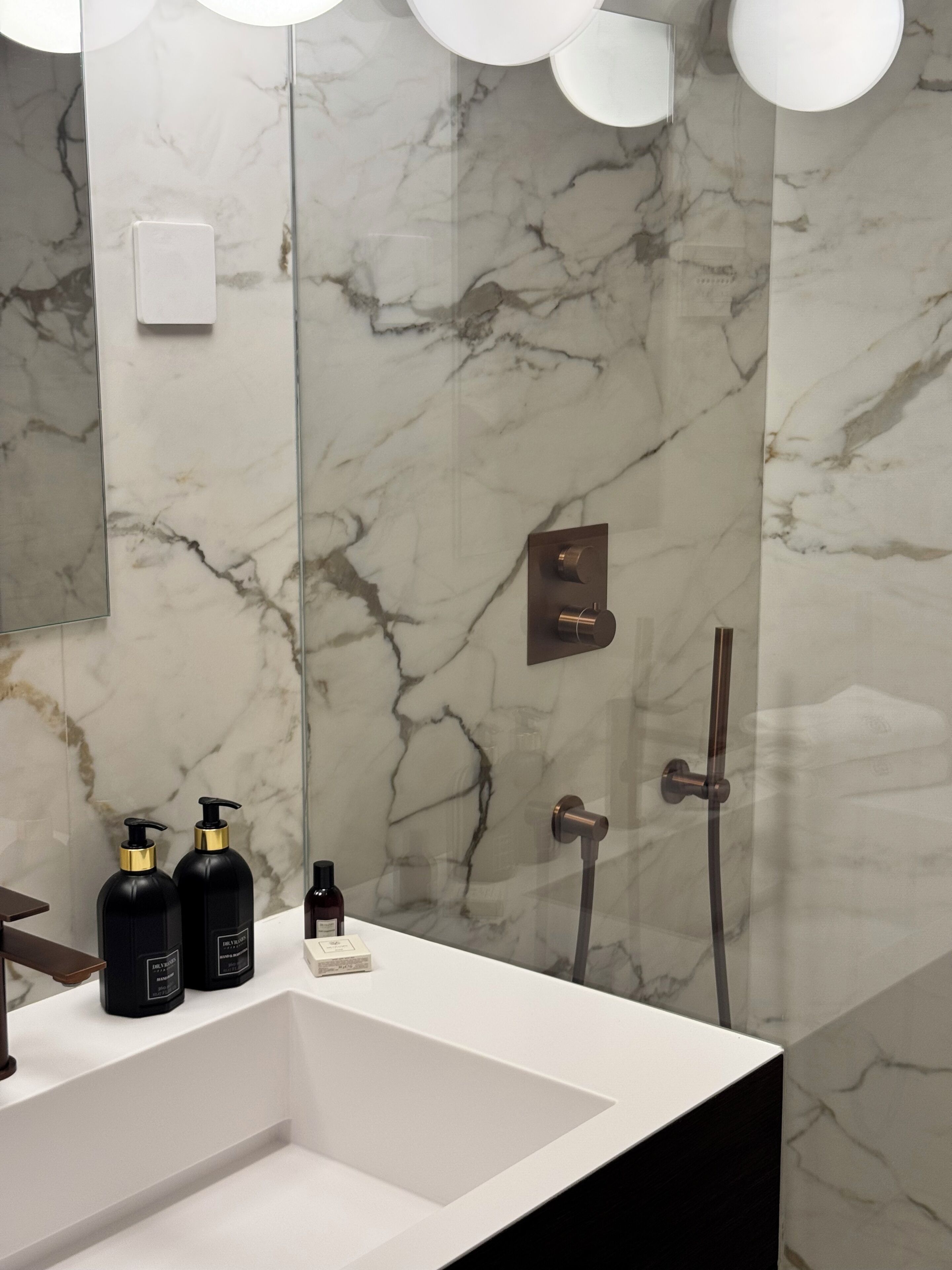 Un baño con pared de mármol, lavamanos y ducha.