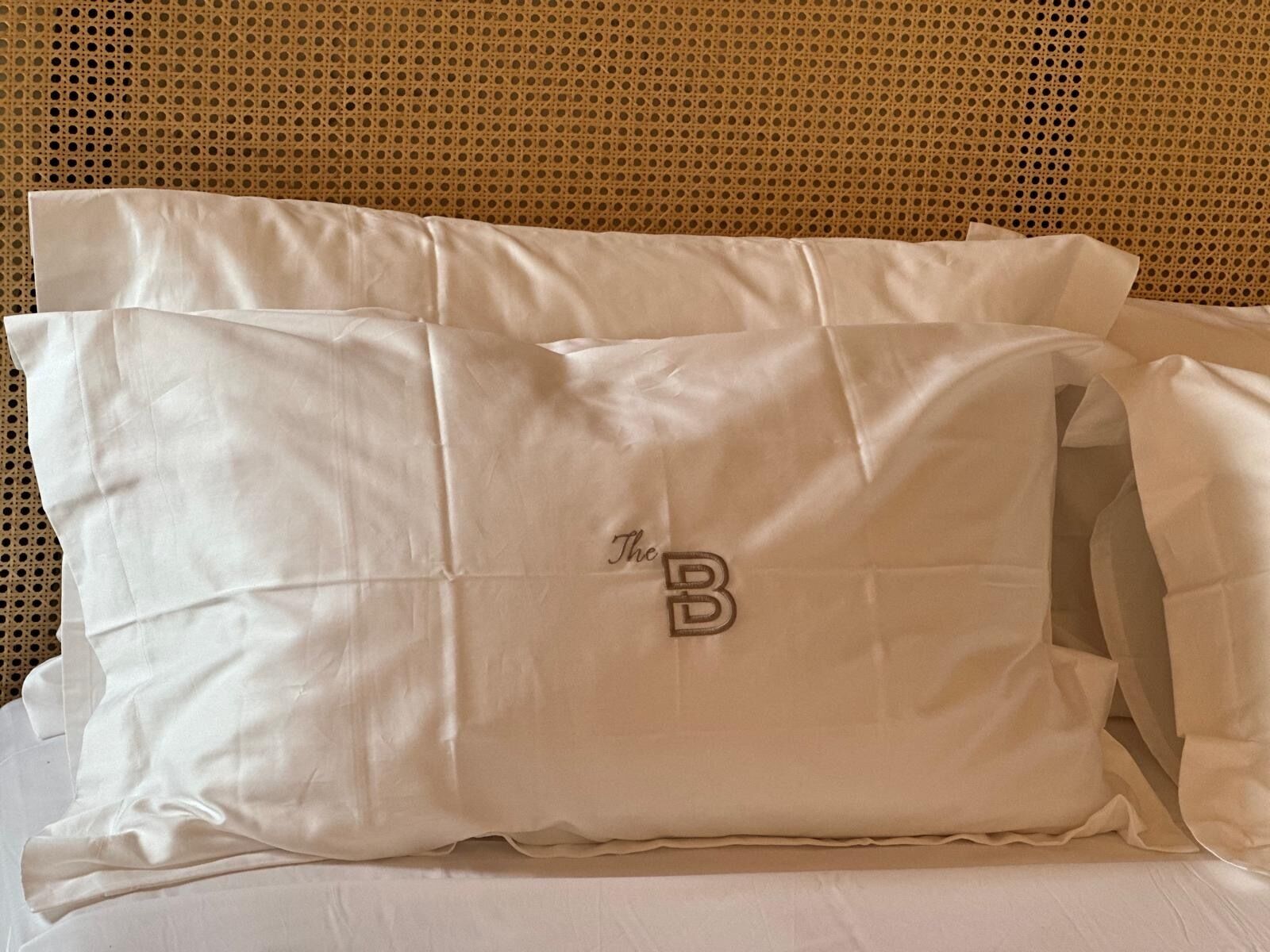 Una cama con dos almohadas blancas y un cabecero tejido.