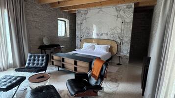 Une chambre à coucher moderne avec un lit, deux fauteuils en cuir, une petite table et un mur en pierre.