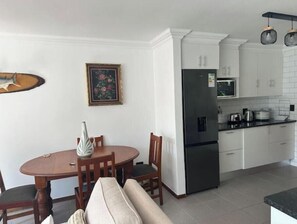 Eine kleine Küche mit weißen Schränken, einem schwarzen Kühlschrank, einer Mikrowelle und einem Essbereich mit einem Holztisch und Stühlen.
