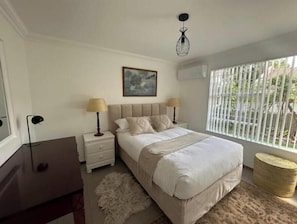 Ein Schlafzimmer mit einem Bett, Nachttischlampen, einem Gemälde und einem Fenster mit Jalousien.