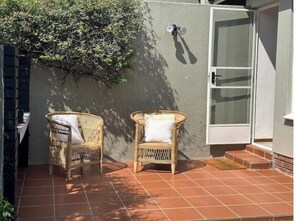 Eine Terrasse mit zwei Korbstühlen und einer weißen Tür.