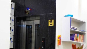 Ascensore con il simbolo del WiFi, una pianta in vaso e una libreria con libri.
