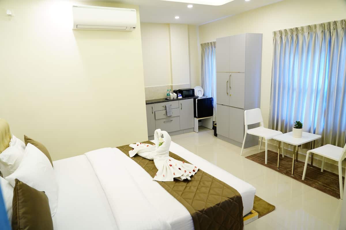 A hotel room with a bed, a small kitchenette, a seating area, and a TV.