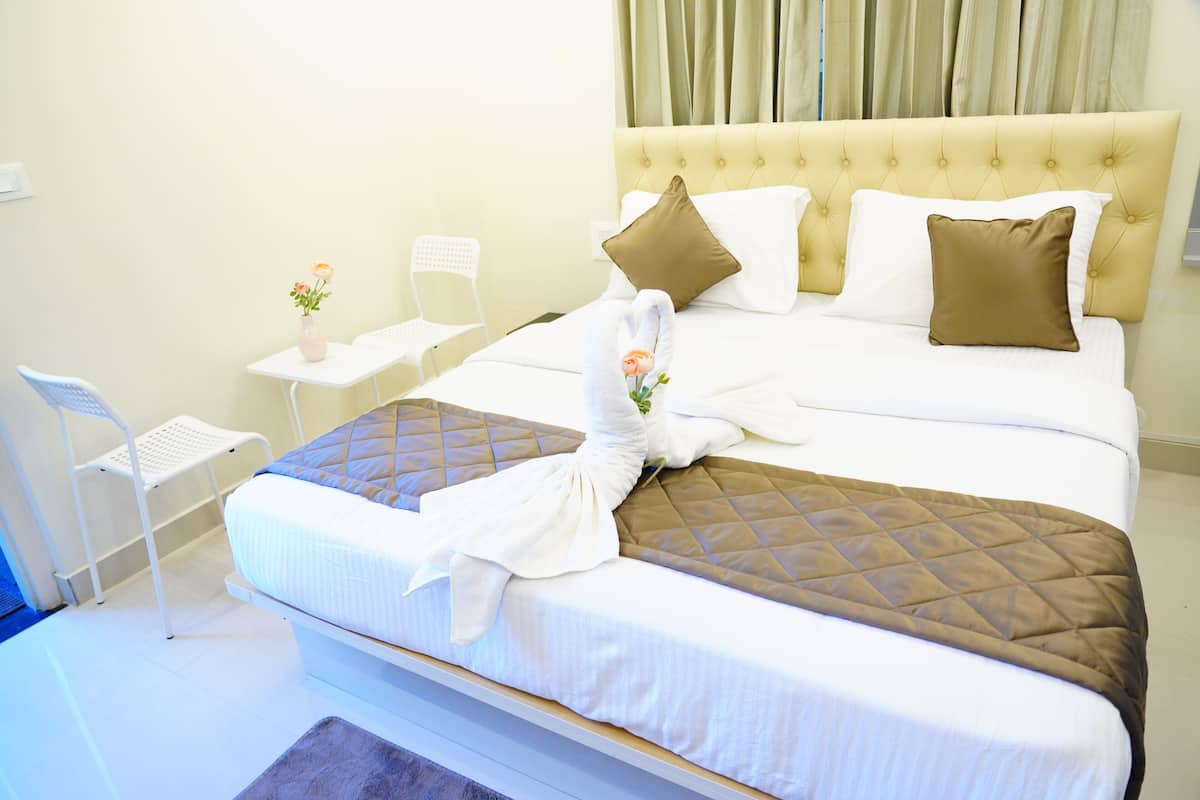 A neatly made bed with a quilted headboard, a bedside table with a vase of flowers, and a chair.