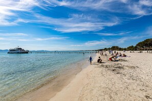 Ein Strand mit klarem Wasser, einer Mole und Menschen, die in der Sonne entspannen.
