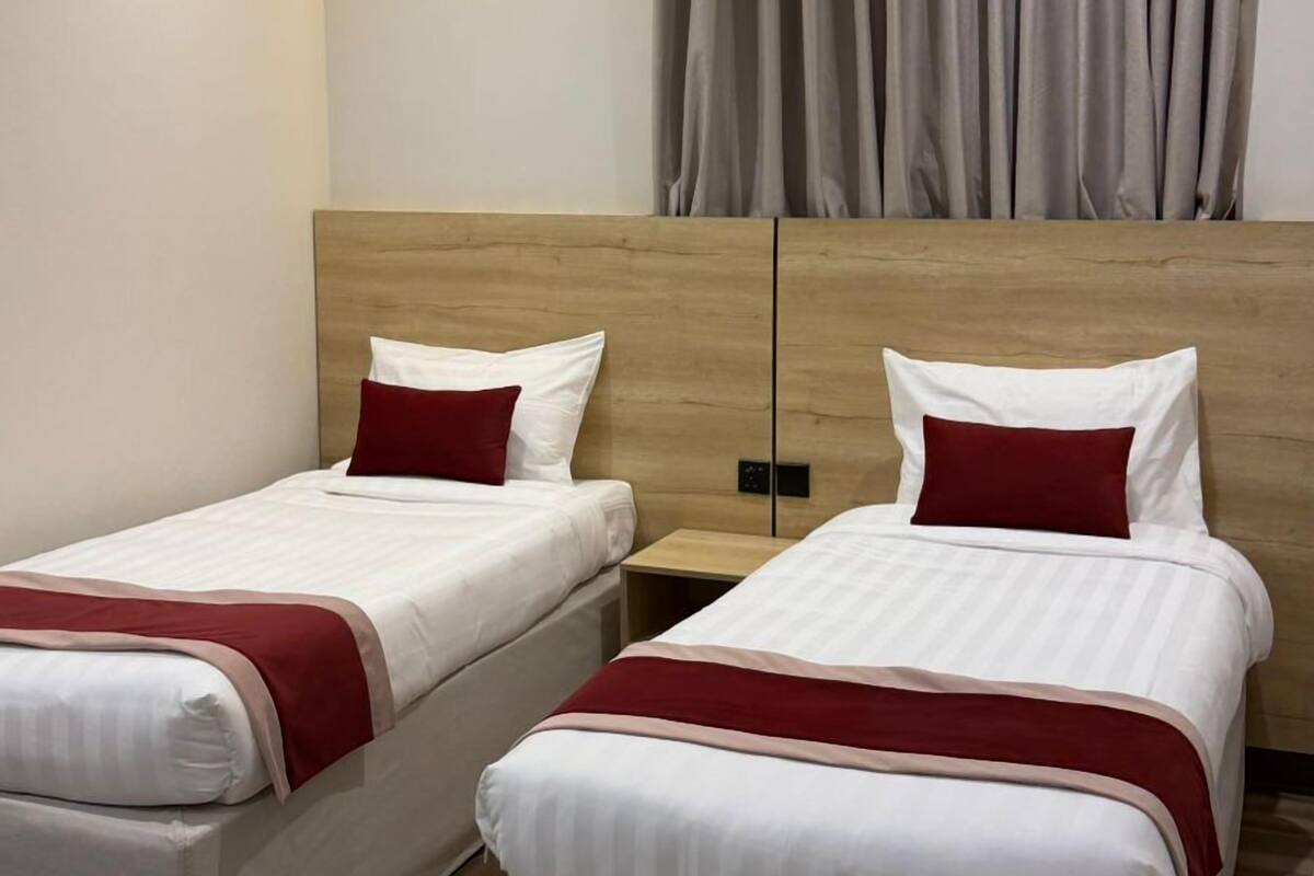 Habitación de hotel con dos camas individuales, cabecera de madera, mesita de noche y un ventanal con cortinas.