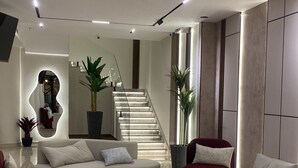 En moderne stue med en buet, hvid sofa, røde lænestole, en stor stueplante og en trappe, der fører til et andet niveau.