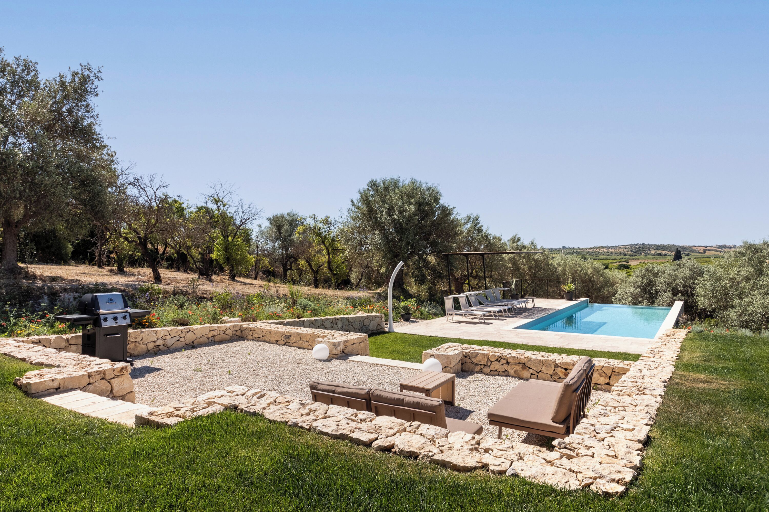 A backyard with a pool, outdoor seating, and a grill.