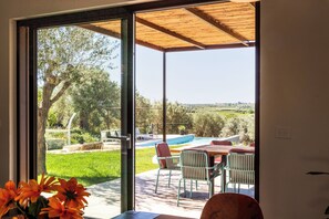 A room with a sliding glass door leading to an outdoor patio with a pool, seating area, and greenery. - Villa Maddalena - Three Bedroom Villa, Sleeps 6 (Noto)