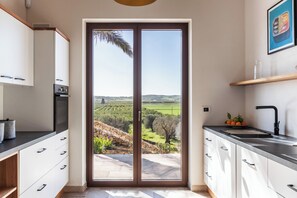A kitchen with a sliding glass door leading to a patio with a view of a green landscape. - Villa Maddalena - Three Bedroom Villa, Sleeps 6 (Noto)