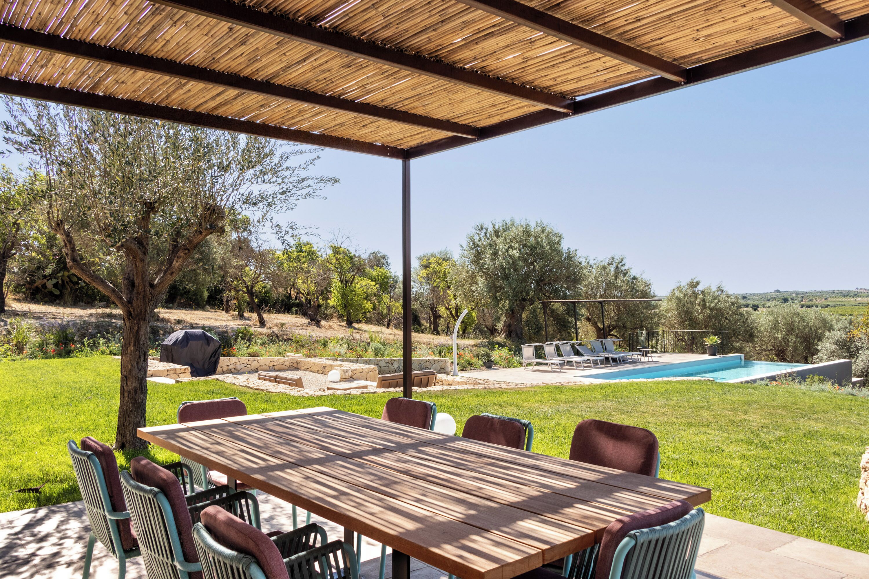 Une terrasse extérieure avec une table et des chaises en bois, un barbecue et une piscine.