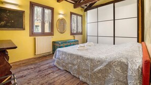 A bedroom with a wooden ceiling, a bed with a lace bedspread, a dresser, a window with curtains, and a radiator. - Cà Leon, Artist’s Loft in the Heart of the City (Venezia)