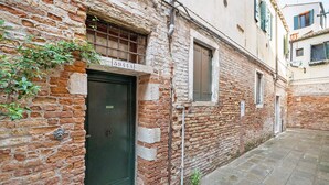 A narrow alleyway with a brick building, a door with a sign, and a window with shutters. - Cà Leon, Artist’s Loft in the Heart of the City (Venezia)