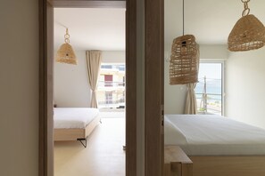 A bedroom with a bed, a window with a view, and a hanging light fixture. - Elegant seafront 2BR apartment, stunning sea views, just steps to shore! (Oropioi)