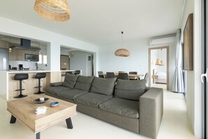 A modern living room with a sofa, coffee table, and dining area. - Elegant seafront 2BR apartment, stunning sea views, just steps to shore! (Oropioi)
