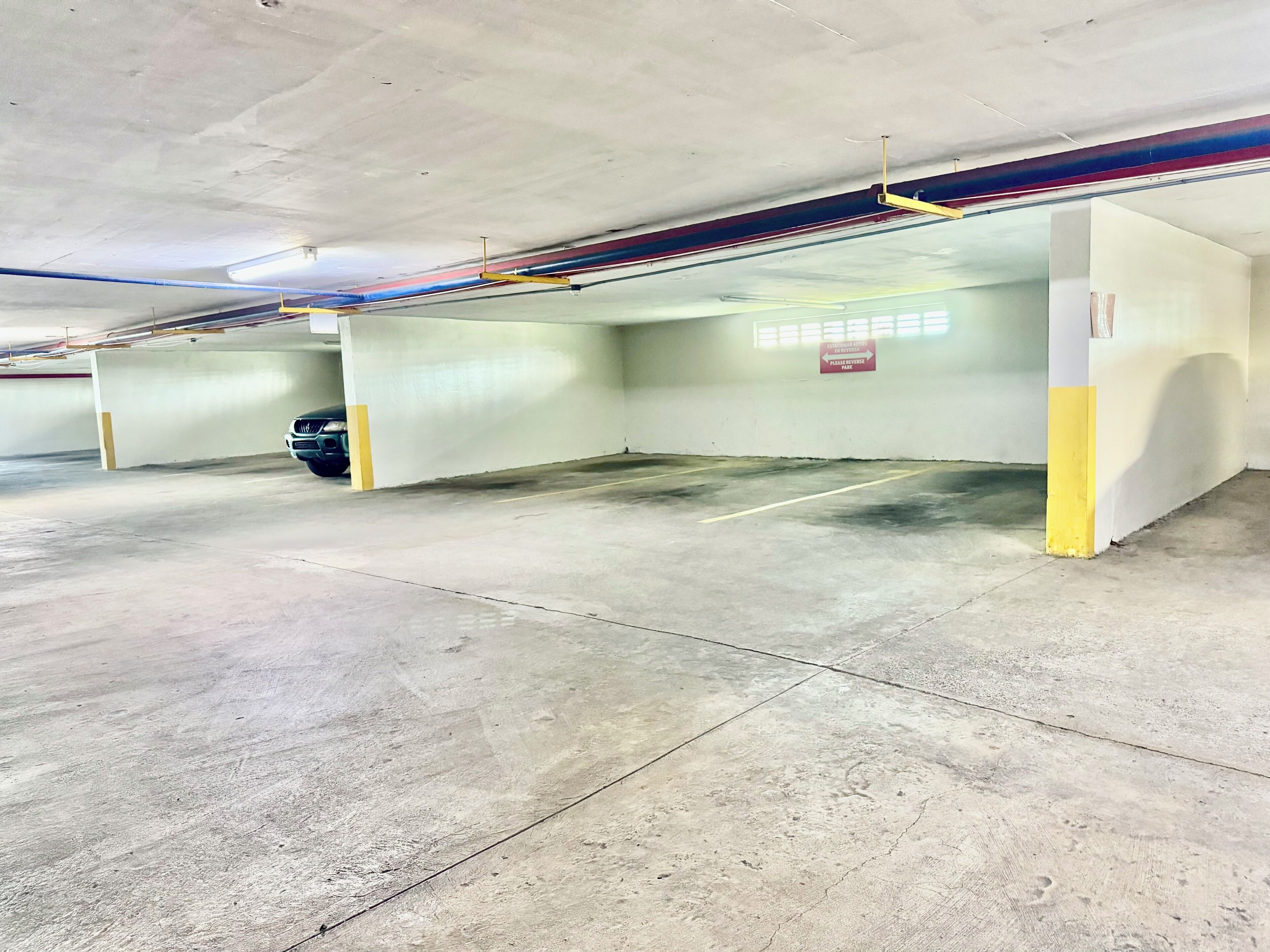 Un parking souterrain avec des planchers en béton, des piliers jaunes et un panneau indiquant une place de stationnement.