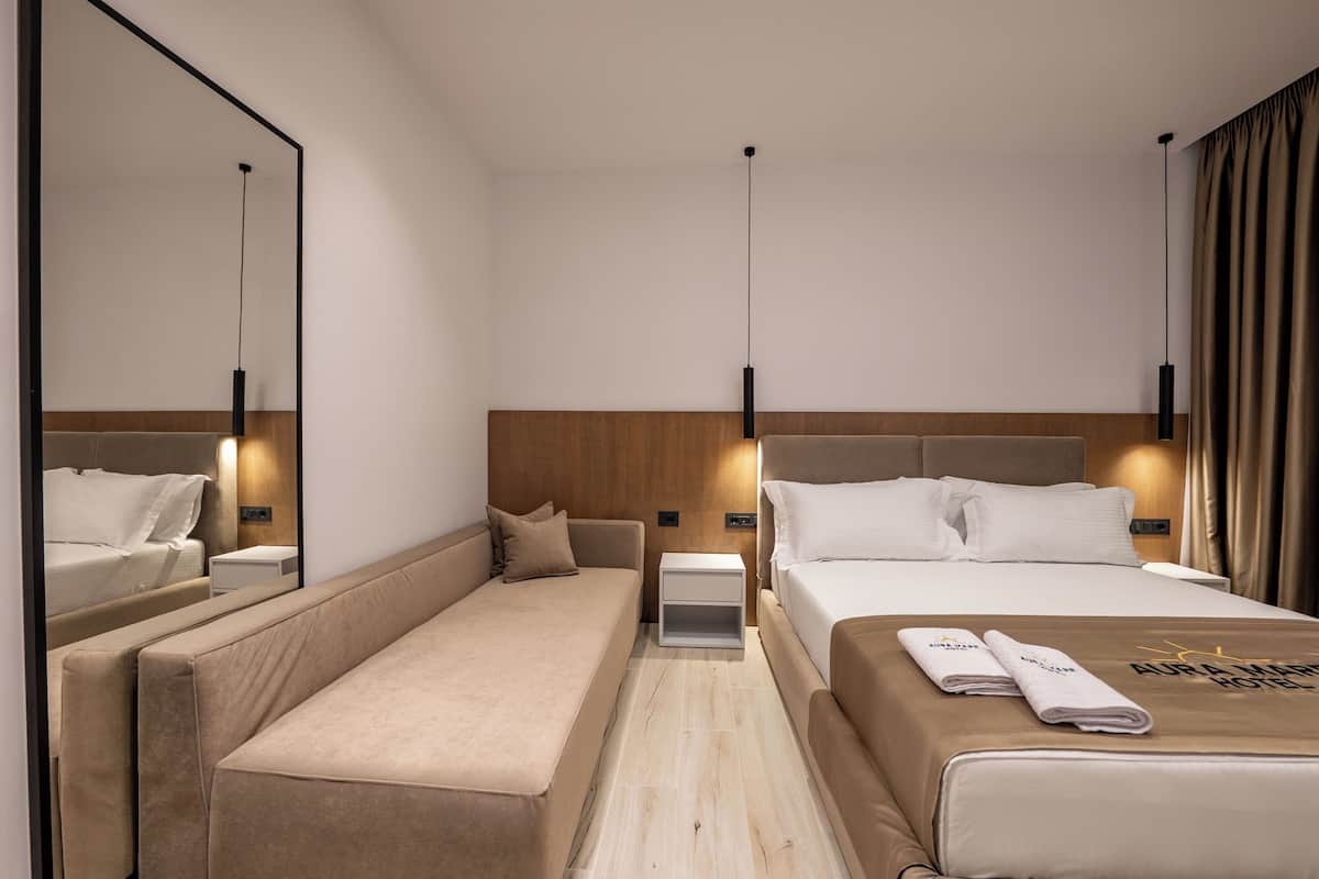A hotel room with a bed, a bench, a nightstand, and a mirror.