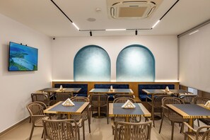Un restaurant doté de nombreuses tables et de banquettes, d’un téléviseur fixé au mur et d’un appareil de climatisation installé au plafond.
