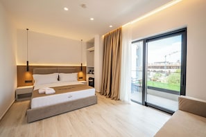 Een moderne hotelkamer met een groot bed, nachtkastjes, en uitzicht op de omgeving door een glazen schuifdeur, plus een balkon.