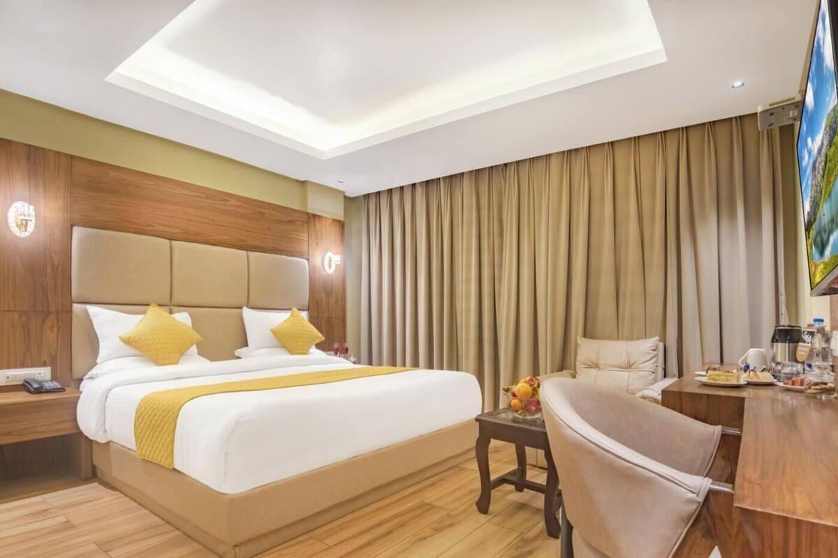 A hotel room with a large bed, a desk with a chair, a television, and a window with curtains.
