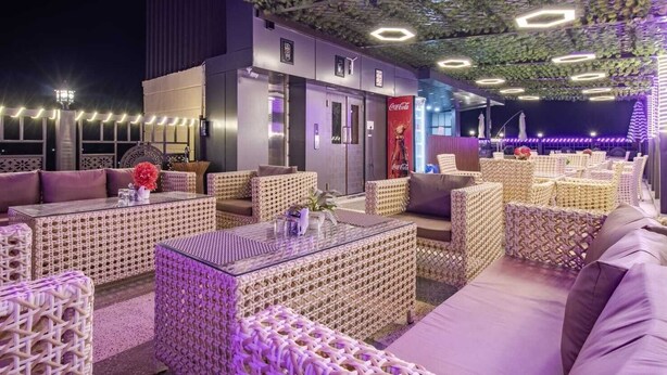 An outdoor seating area with wicker furniture and a Coca-Cola advertisement. - Sondermall Palace (Srinagar)