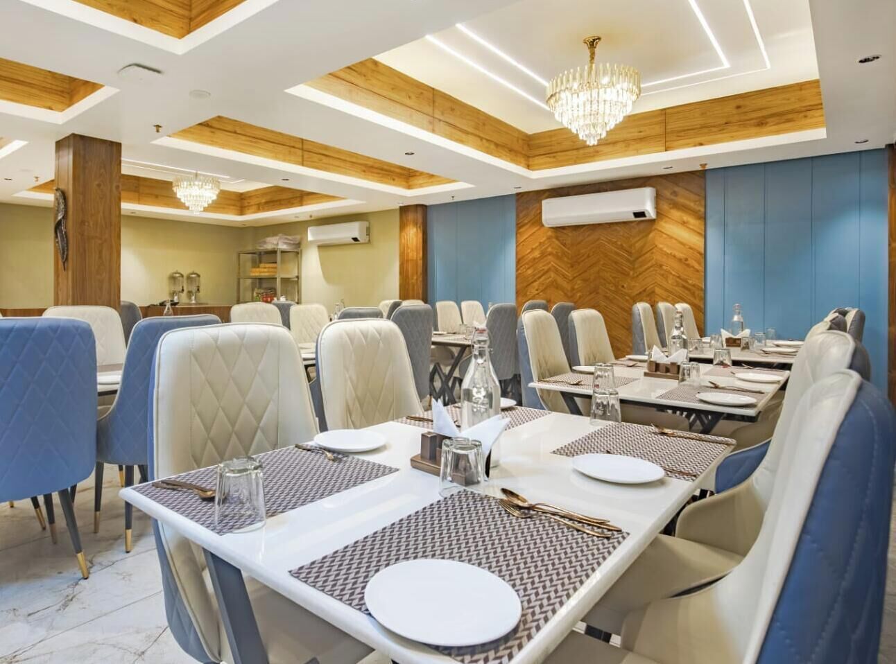 A dining area with tables set for service, a chandelier, and a herringbone-patterned wall.