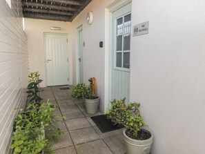 A narrow corridor with potted plants, a door labeled '102 The Bolthouse,' and a small window with a metal grill. - The Bolthole (Newport)