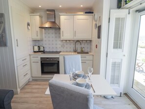 A compact kitchen with white cabinetry, a built-in oven, and a stainless steel range hood. - The Bolthole (Newport)