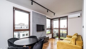En moderne stue med spiseområde, store vinduer, et fladskærms-tv og en gul sofa.