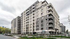 En flere etagers boligbygning med altaner, et skilt med 'Fair Play' og en parkeringsplads foran.