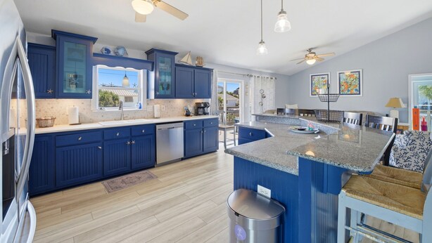 A modern kitchen with blue cabinets, a granite countertop, and a ceiling fan. - Family Fun Minutes from the Waters Edge (Pensacola Beach)