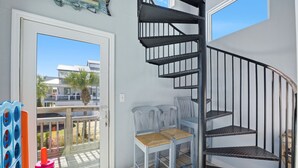A room with a spiral staircase, a balcony with a view of buildings and palm trees, and a door leading outside. - Family Fun Minutes from the Waters Edge (Pensacola Beach)