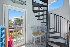 Quarto com escada em espiral, varanda com vista para edifícios e palmeiras, e porta que dá para o exterior.