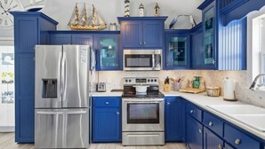 A kitchen with blue cabinets, stainless steel appliances, and nautical decorations. - Family Fun Minutes from the Waters Edge (Pensacola Beach)