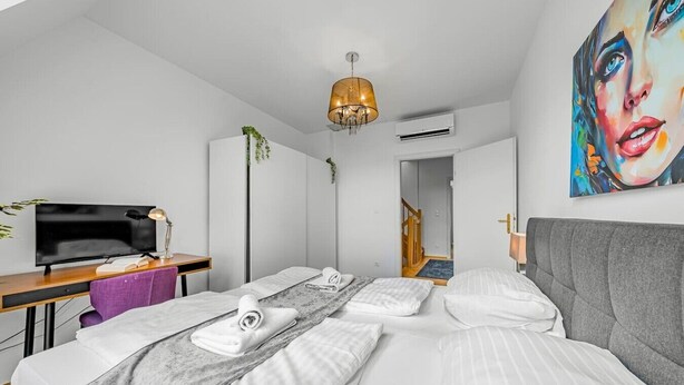 Een moderne hotelkamer met een bed, een bureau met een televisie, een kroonluchter en een schilderij aan de muur.