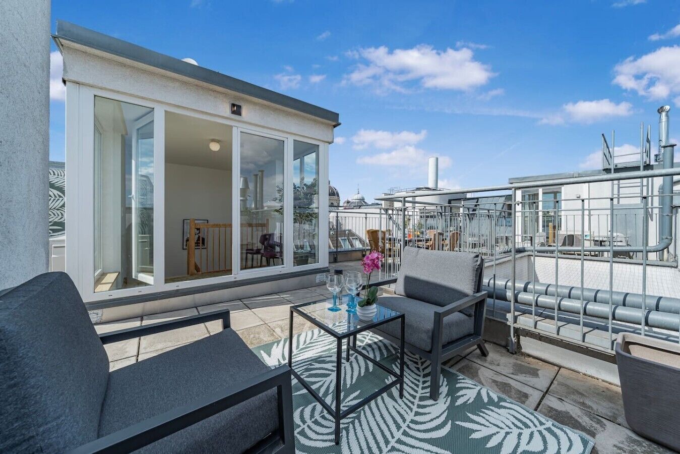 A rooftop terrace with outdoor seating, a glass door entrance, and a view of the cityscape.