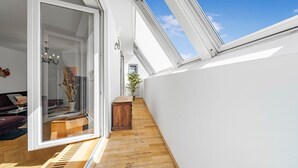 Een smalle gang met houten vloer, een glazen deur naar een kamer met een kroonluchter, en een kleine houten tafel.