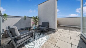 Een dakterras met een bank, fauteuil en een kleine tafel met een bloevas.