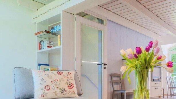 A living room with a sofa, a coffee table, a bookshelf, and a vase with flowers. - Vacation apartment Stöfs - Baltic Sea vacation. Close to the beach. Nature. Lake view. (Behrensdorf)