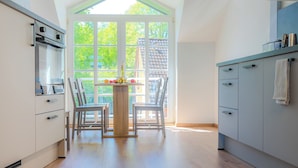 A modern kitchen with a dining table, chairs, and a large window. - Vacation apartment Stöfs - Baltic Sea vacation. Close to the beach. Nature. Lake view. (Behrensdorf)