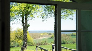 A room with a large window offering a view of a tree-lined landscape and a body of water. - Vacation apartment Stöfs - Baltic Sea vacation. Close to the beach. Nature. Lake view. (Behrensdorf)