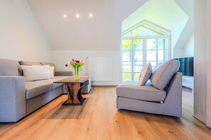Ein modernes Wohnzimmer mit einer Couch, einem Sessel und einem kleinen Tisch mit einem Blumenstrauß.